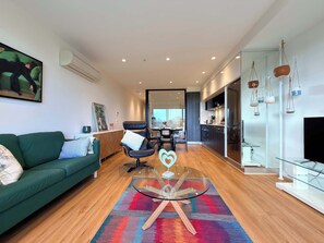 Ein modernes Wohnzimmer mit einem grünen Sofa, einem Glastisch und einem bunten Teppich.