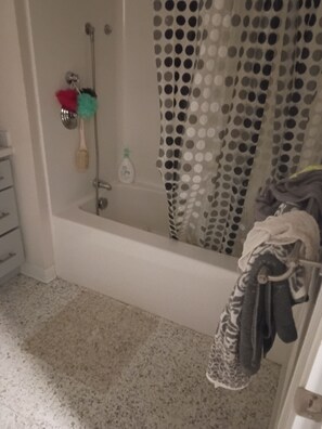 Un baño con bañera, cortina de ducha con estampado de lunares, toallero con toalla y una botella de champú.