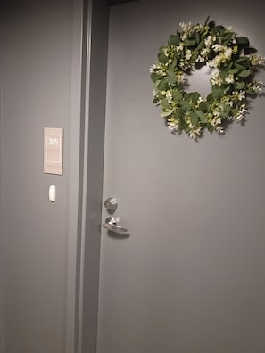 Una puerta con una placa de número, un picaporte y un adorno de guirnalda.
