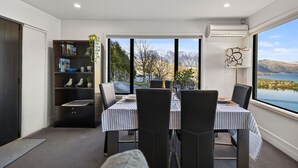Uma área de refeições com uma mesa posta para quatro pessoas, uma estante de livros e vista para um lago e montanhas.