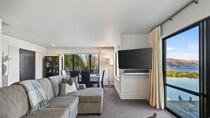 Uma sala de estar moderna com um sofá, uma televisão de tela plana e um espaço de jantar com mesa e cadeiras.