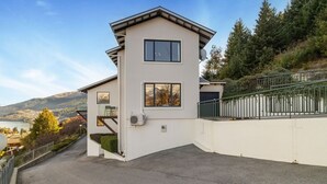 Uma casa moderna de dois andares com varanda, antena parabólica e vista para um lago e montanhas.