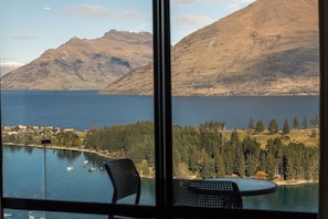 A room with a large window overlooking a lake, mountains, and a forested area.
