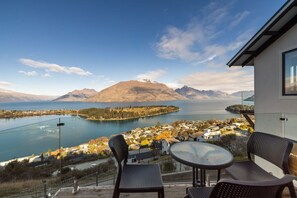 A balcony with a table and chairs overlooking a lake and mountains.