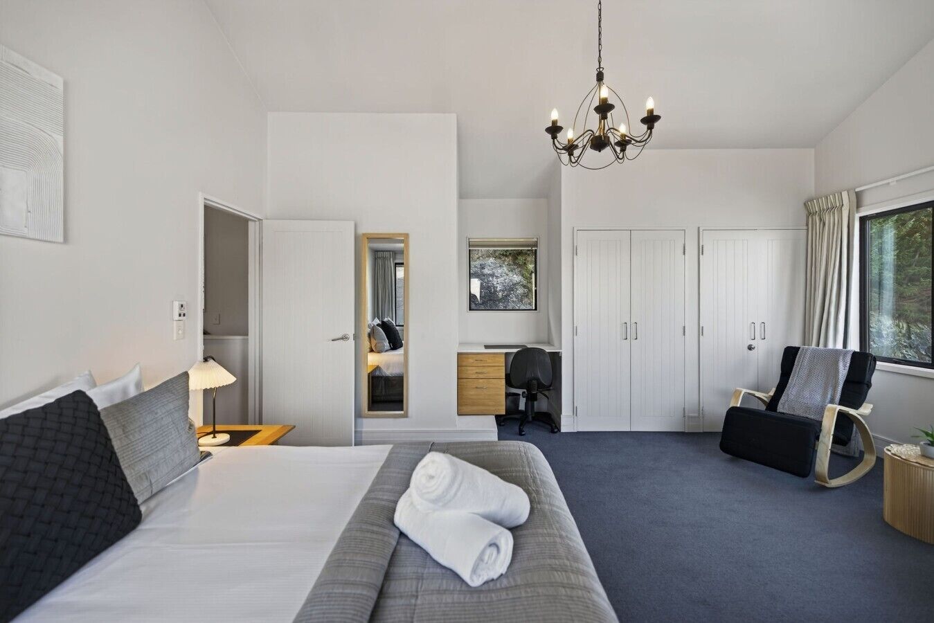Habitación de hotel con cama, escritorio, silla, armario y candelabro.