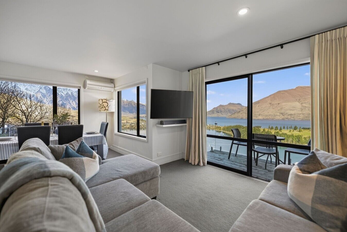 A modern hotel room with a large bed, a dining area, and a balcony with a scenic mountain view.
