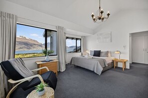 A hotel room with a bed, a desk, a chair, a bedside table, a lamp, and a view of a mountain and lake. - Jaw Dropping Views, Close To The Heart Of Queenstown (Queenstown)