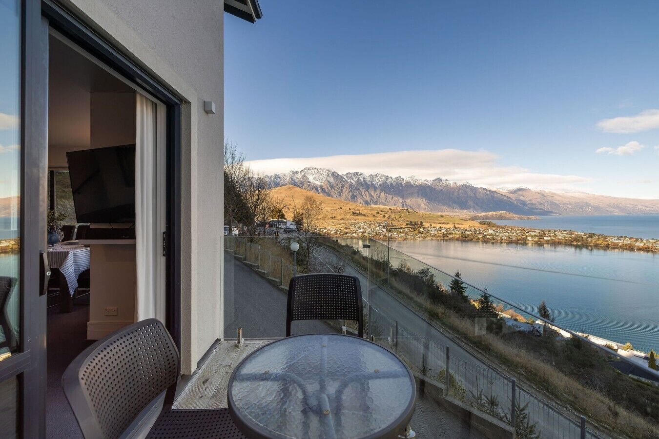 Un balcon avec une table et des chaises, donnant sur un lac et des montagnes.