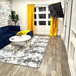 A room with a blue sofa, a round coffee table with a plant, a fluffy rug, and a TV mounted on the wall. - Serene 3-bedroom apartment with AC in Atlanta (Atlanta)