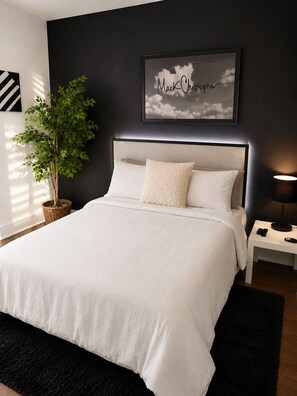 Un dormitorio moderno con una cama grande, una mesita de noche con lámpara y un cuadro enmarcado en la pared.