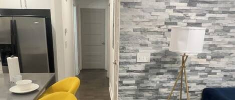 Eine moderne Küche mit Einbaukühlschrank, ein Essbereich mit gelben Stühlen und eine Wand mit grauem Steinmuster.