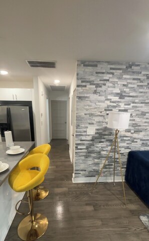 A modern kitchen with a built-in refrigerator, a dining area with yellow chairs, and a wall with a gray stone pattern.