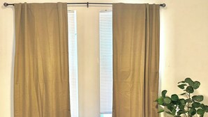 Una ventana con cortinas color beige y una planta en maceta a su lado.