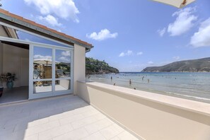 Ein Balkon mit Blick auf Strand und Meer, ein Blumentopf und eine Person mit Kamera.