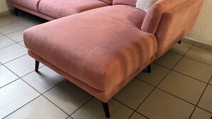 A pink sectional sofa with a footstool and two pillows against a wall with abstract art.