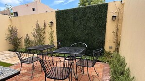 An outdoor patio with a table and chairs, a green hedge, and a tiled floor. - CM House with Parking (Hermosillo)