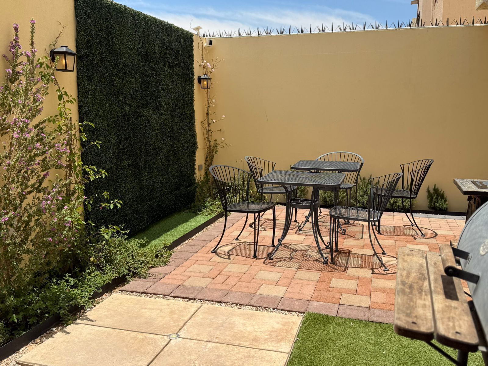 Un patio al aire libre con una mesa y sillas, un seto y una pared.