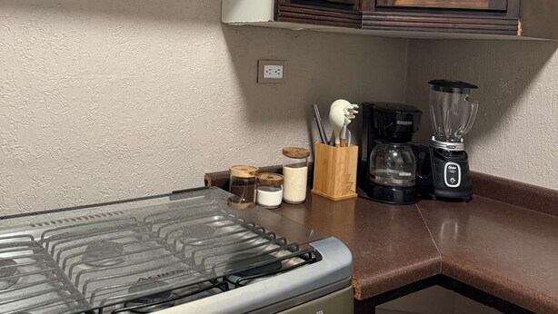 A kitchen with a gas stove, a coffee maker, a blender, and wooden cabinets.