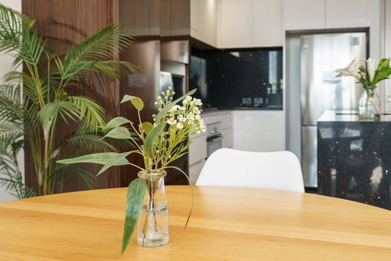 Ein Holztisch mit einer klaren Glasvase, gefüllt mit weißen Blumen und grünen Blättern.