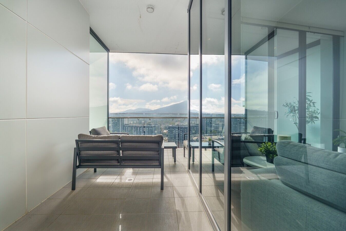 A modern living room with a sofa, a coffee table, and a view of a cityscape through large windows.