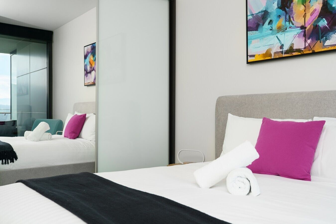 Una habitación de hotel con una cama, almohadas, una colcha, un espejo y un cuadro en la pared.