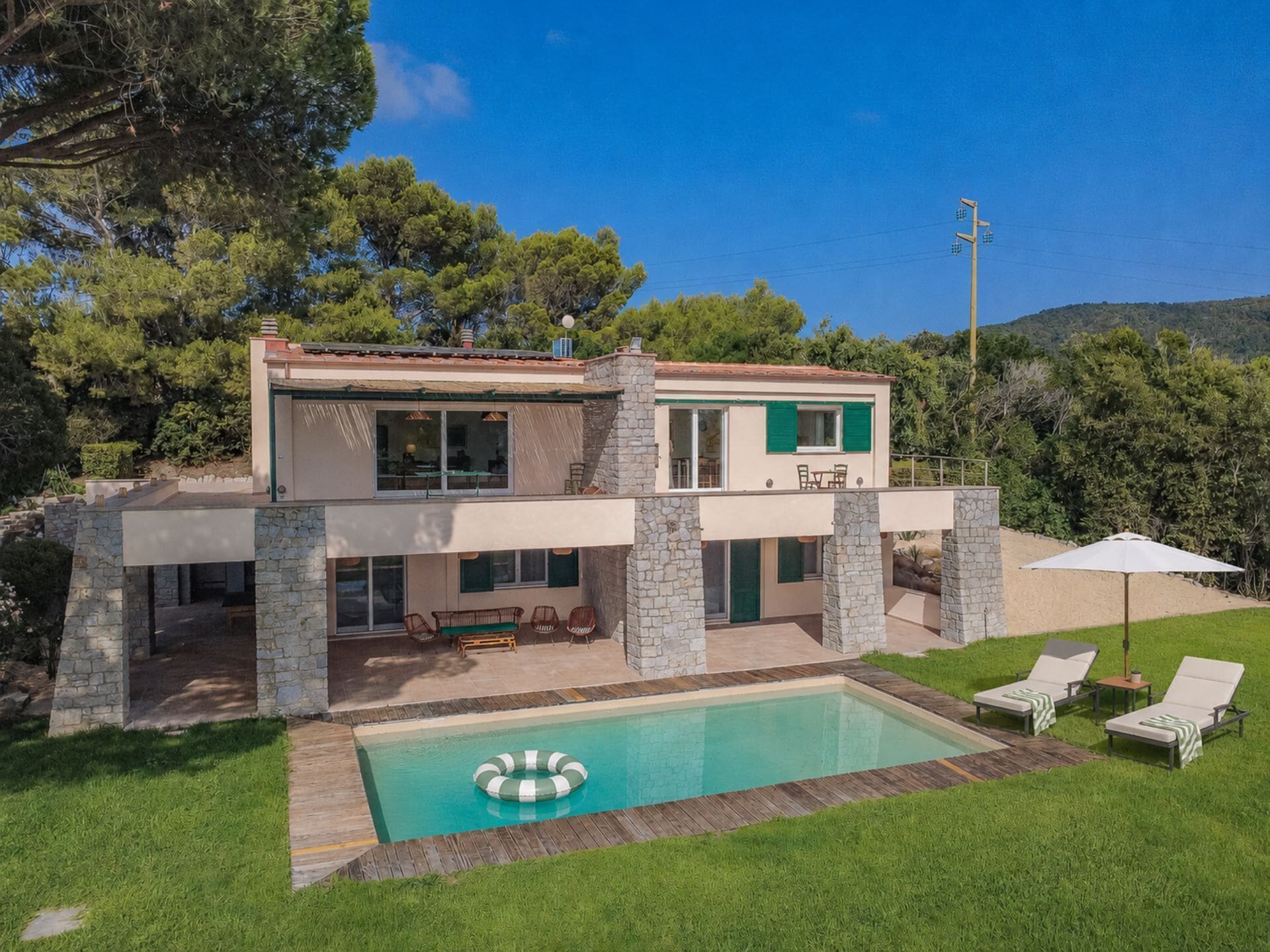 A two-story house with a swimming pool, outdoor seating, and a view of the surrounding landscape.