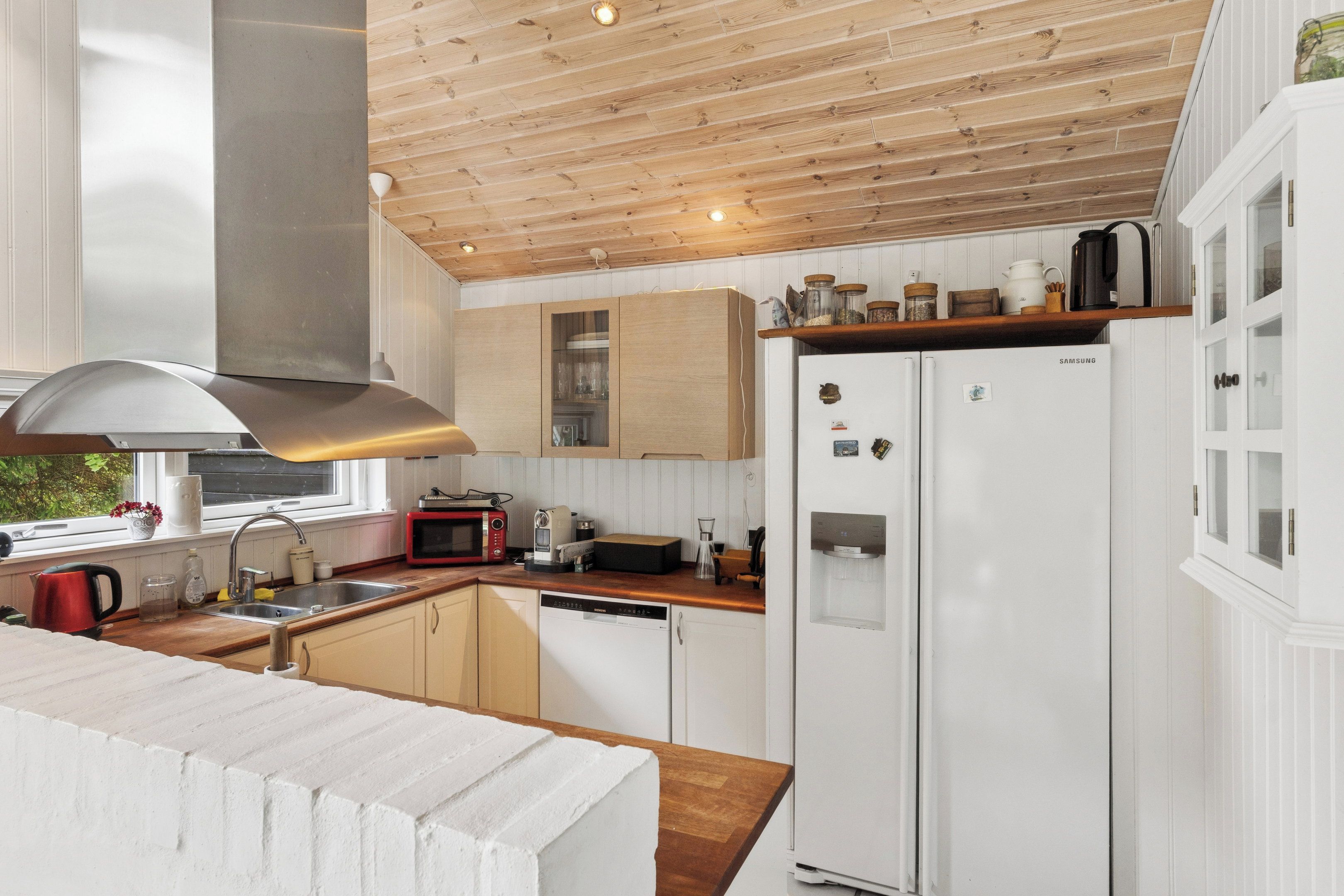 Een moderne keuken met houten balken in het plafond, witte keukenkastjes, een roestvrijstalen afzuigkap en een geïntegreerde waterdispenser.