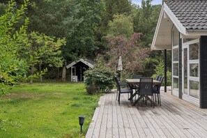 Eine Holzterrasse mit Tisch und Stühlen, umgeben von üppigem Grün und einer kleinen Holzkonstruktion.