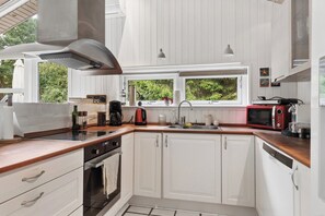 Une cuisine moderne avec des meubles blancs, une hotte de cuisinière en acier inoxydable et une fenêtre donnant sur la verdure à l’extérieur.