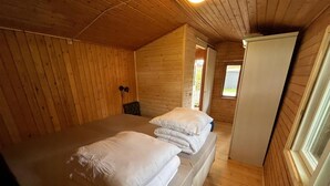 Ein Zimmer einer Holzhütte mit einem Bett, einem kleinen Tisch und einem Fenster.