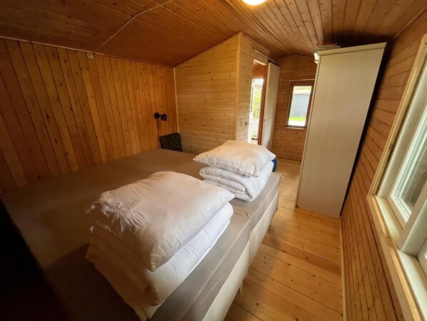 En stuga med träpanel, ett rum med en säng, ett litet bord och ett fönster.