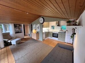 A modern kitchen with white cabinets, a built-in oven, and a dining area with a sofa and a rug. - Aarhus - 100m to beach, 200m to bus (Egå)