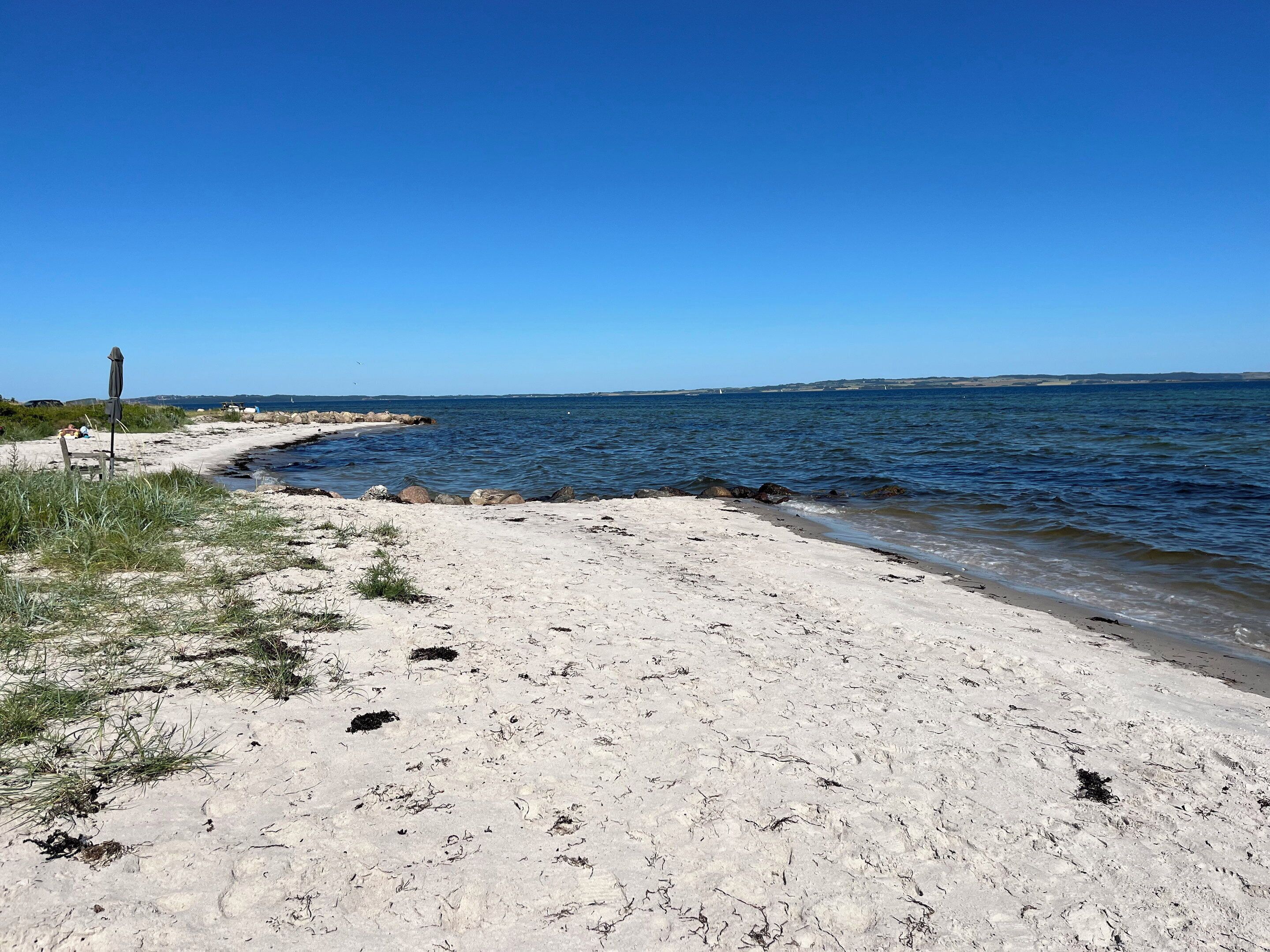 Une plage de sable fin, avec une eau d’un bleu limpide et une terre ferme qui se devine au loin.