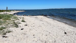 Ein sandiger Strand mit klarem, blauem Wasser und weiter Küste.