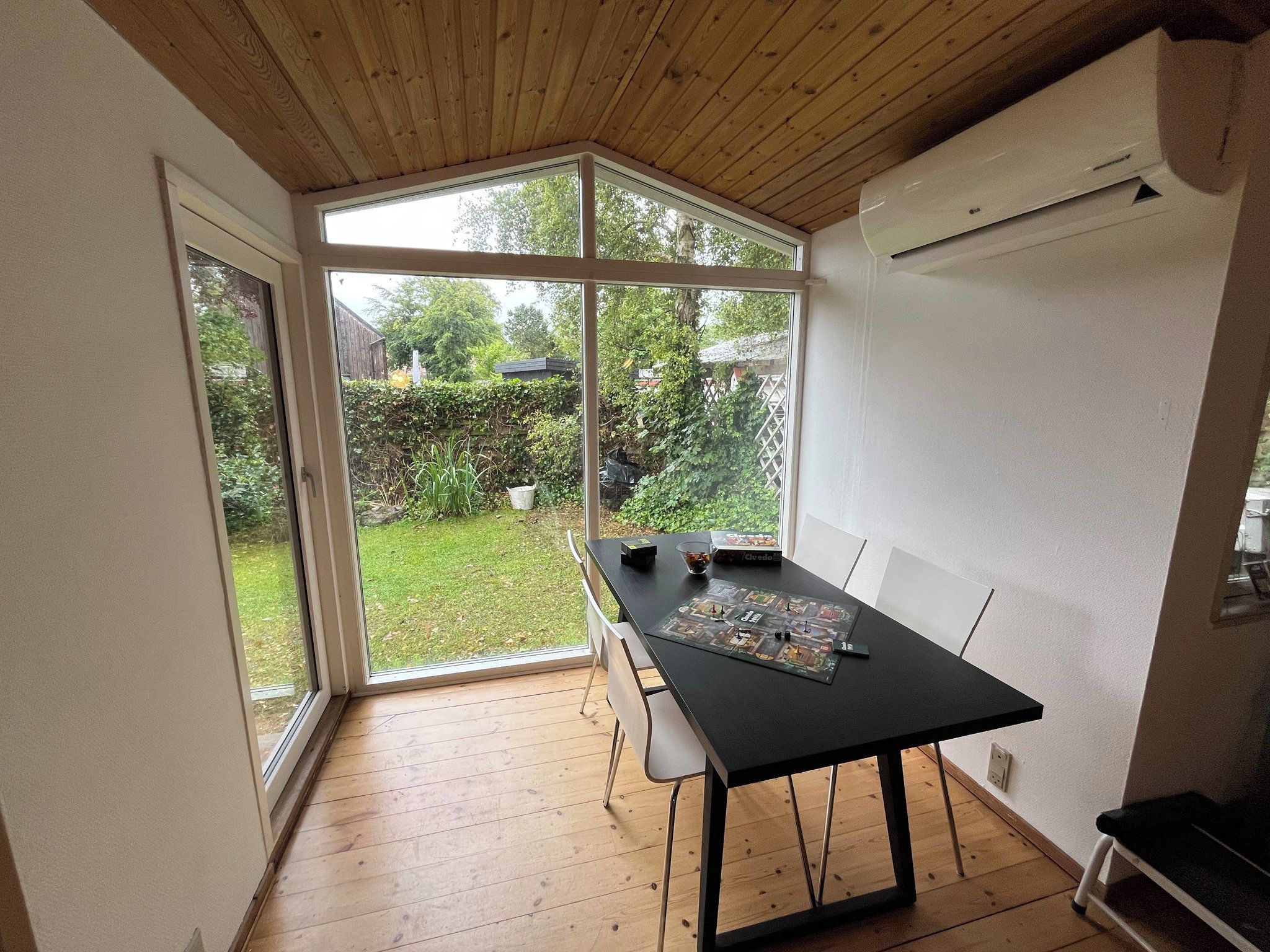 A room with a wooden ceiling, a table with chairs, a window, and an air conditioning unit.