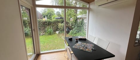 A room with a wooden ceiling, a table with chairs, a window, and an air conditioning unit.