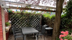 Ein überdachter Patio-Bereich mit Tisch und Stühlen, umgeben von einem Gitterzaun und Pflanzen.