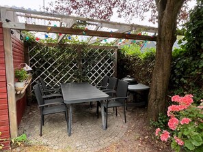 A covered patio area with a table and chairs, surrounded by a lattice fence and greenery. - Aarhus - 100m to beach, 200m to bus (Egå)