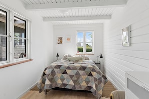 Un dormitorio con cama, ventana y lámpara fijada a la pared.