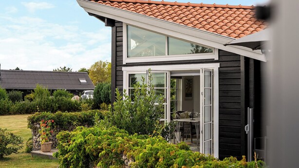 Ett modernt hus med ett tak täckt av takpannor, stora fönster och en välskött trädgård.