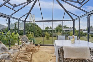Un invernadero con techo de cristal, mobiliario de mimbre y vistas a un jardín.
