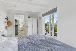 Ein Schlafzimmer mit einem großen Bett, einem Kleiderschrank, einem Kleiderhaken und Blick ins Freie durch eine Schiebetür.