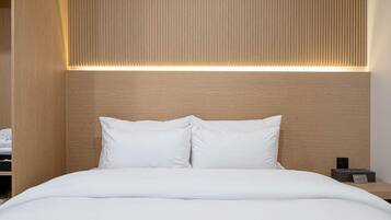 A modern hotel room with a wooden headboard, a neatly made bed with white linens, and a bedside table with a small electronic device.