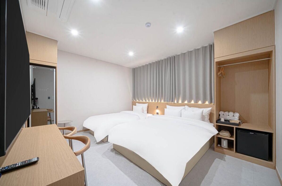 Habitación de hotel con dos camas, un escritorio, una silla, un armario y un televisor pequeño.