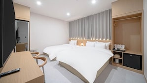 Ein Hotelzimmer mit zwei Betten, einem Schreibtisch, einem Stuhl, einem Kleiderschrank und einem kleinen Fernseher.