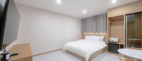 A hotel room with a bed, bedside table, TV, and a small desk with a chair.