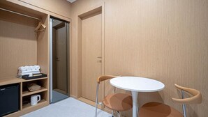 Ein kleines Zimmer mit Kleiderschrank, einem Tisch für zwei Personen sowie einem Regal mit Handtüchern und einer Kaffeemaschine.
