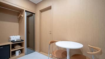 Habitación compacta con armario, una pequeña mesa y dos sillas, y una estantería con toallas y cafetera.