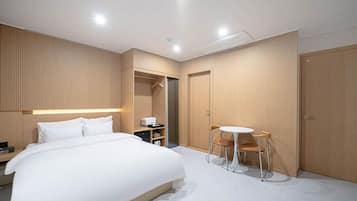 A modern hotel room with a large bed, a bedside table, a wardrobe, a seating area with a table and chairs, and a walk-in closet.