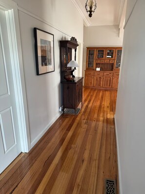 A hallway with wooden flooring, a framed picture on the wall, a lamp, and a cabinet with glass doors. - Newport House 2 bedroom, 1 sofa bed, 1 bathroom (Newport)